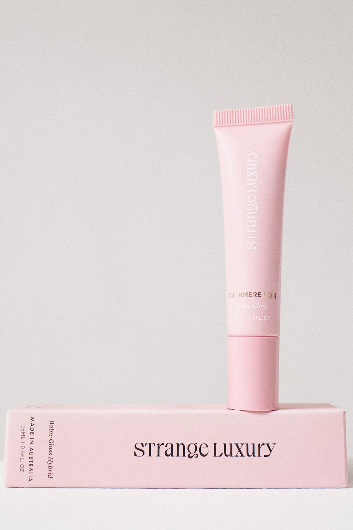 Pink skincare tube and box with 'Strange Luxury' branding on a light gray background