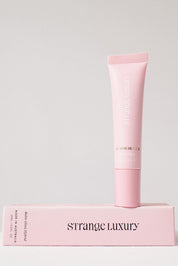 Pink skincare tube and box with 'Strange Luxury' branding on a light gray background