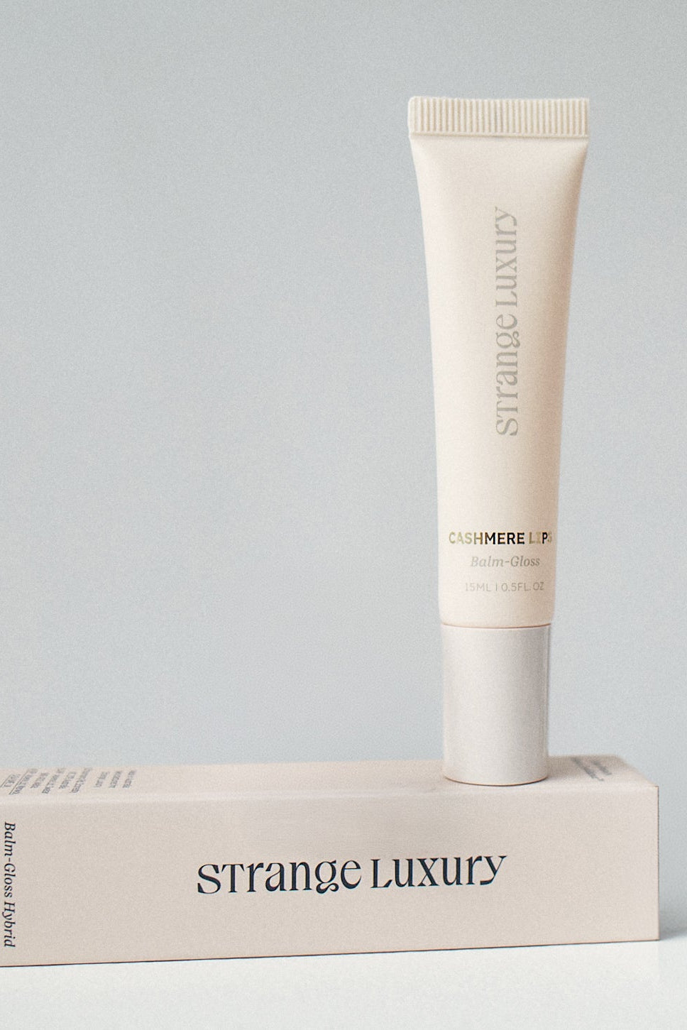 Tube of Strange Luxury skincare product on a matching box against a gray background.