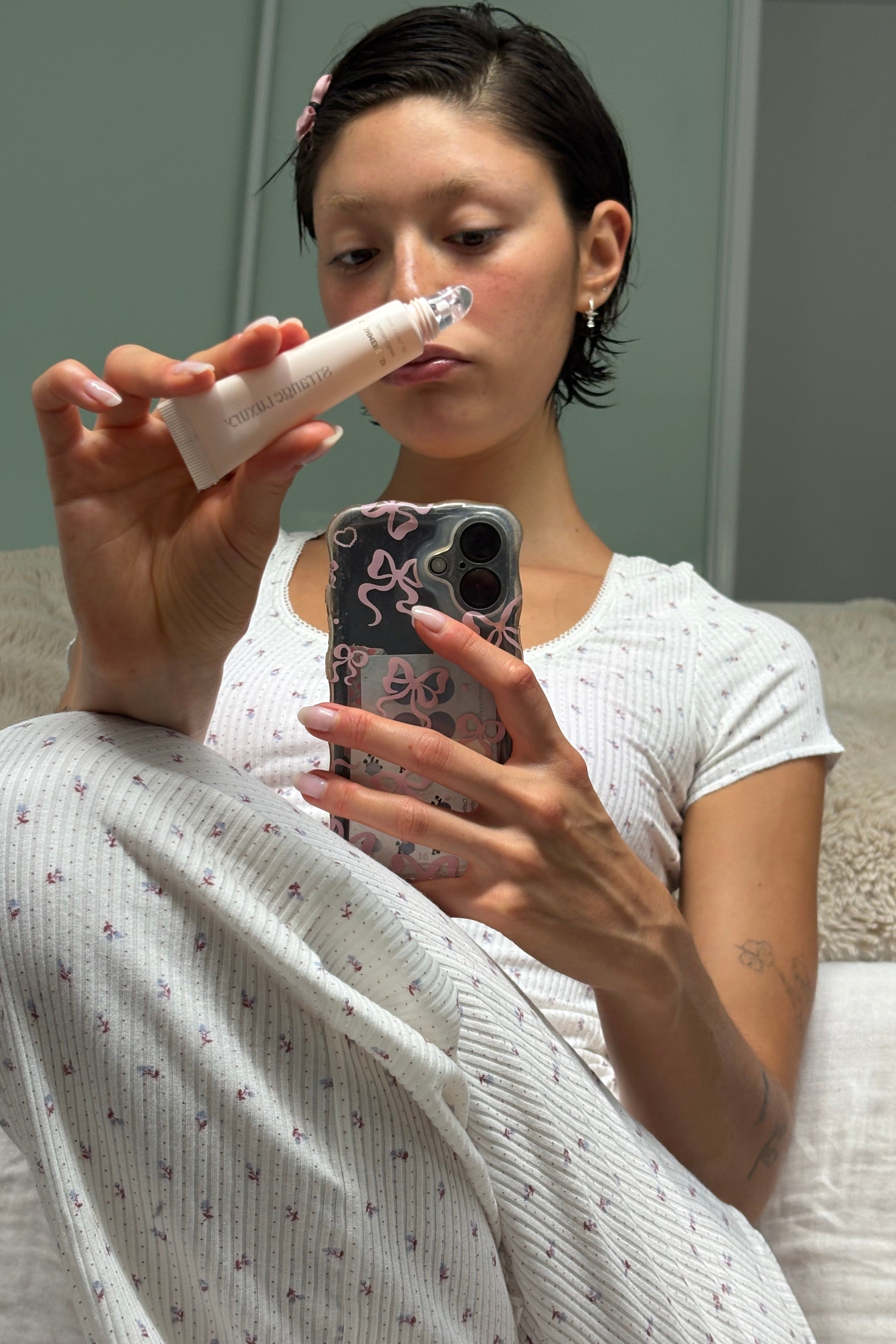Amber using a lip product with a phone in a bedroom setting.