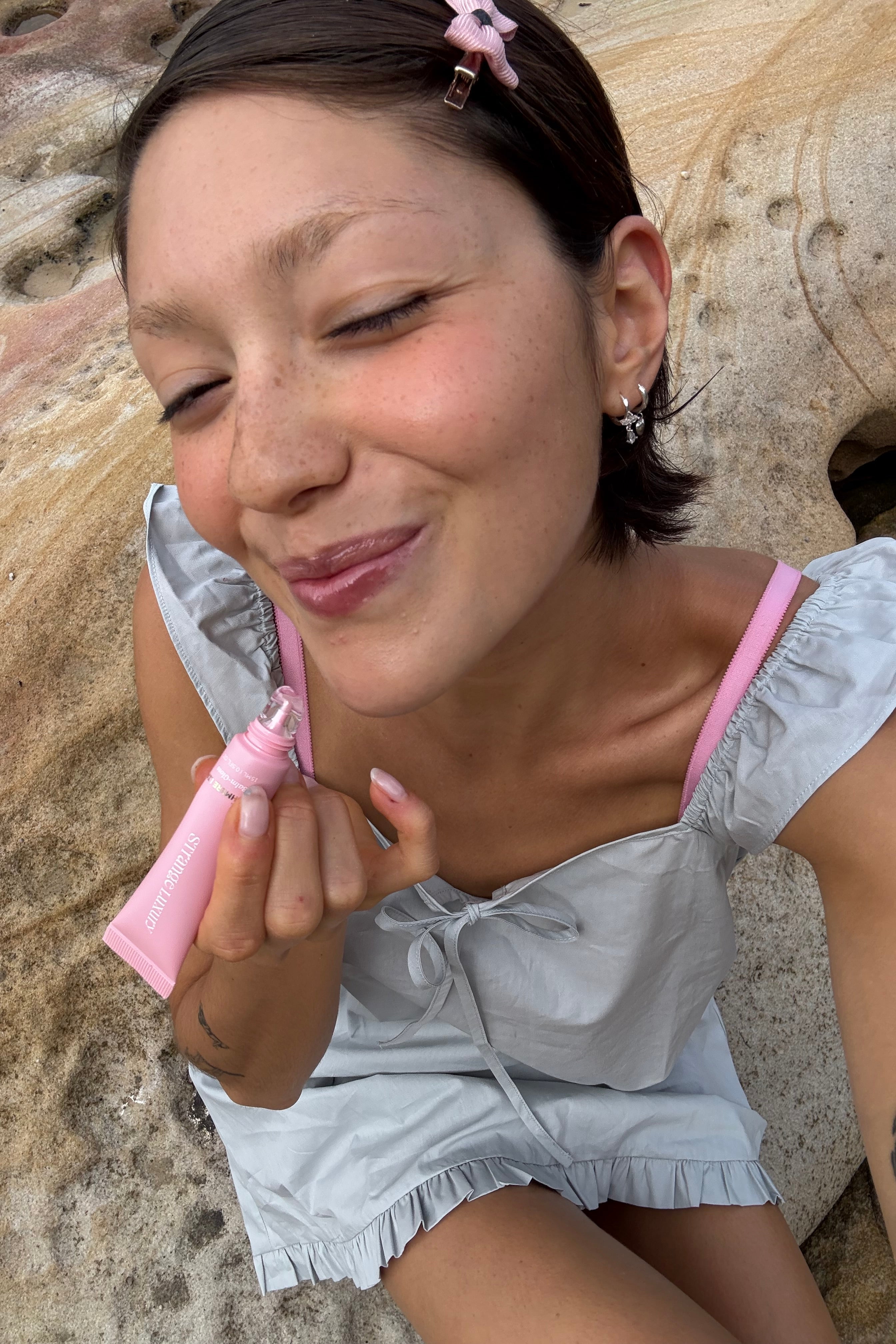 Amber sitting applying lip gloss on stone background.