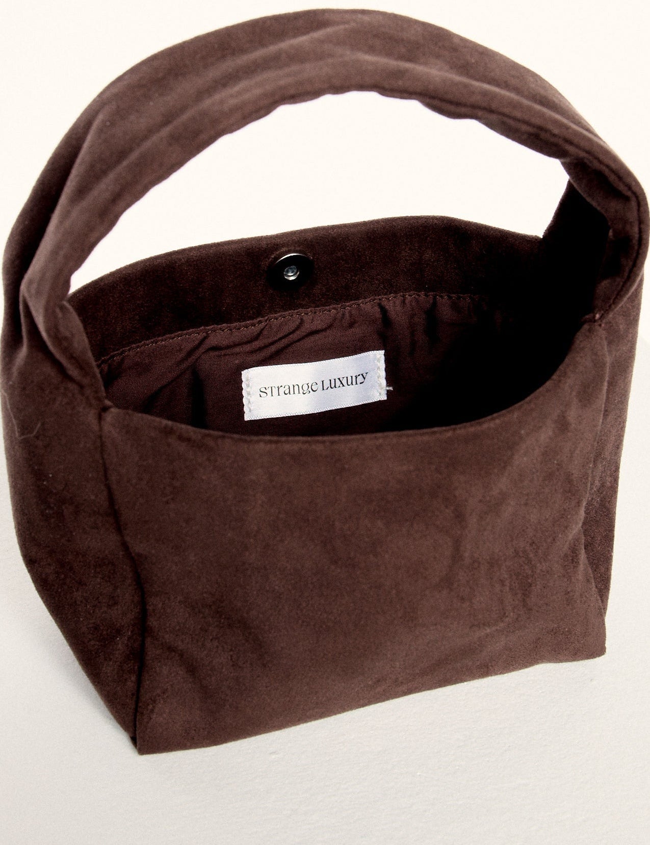 Brown suede handbag with a visible brand label on a white background.