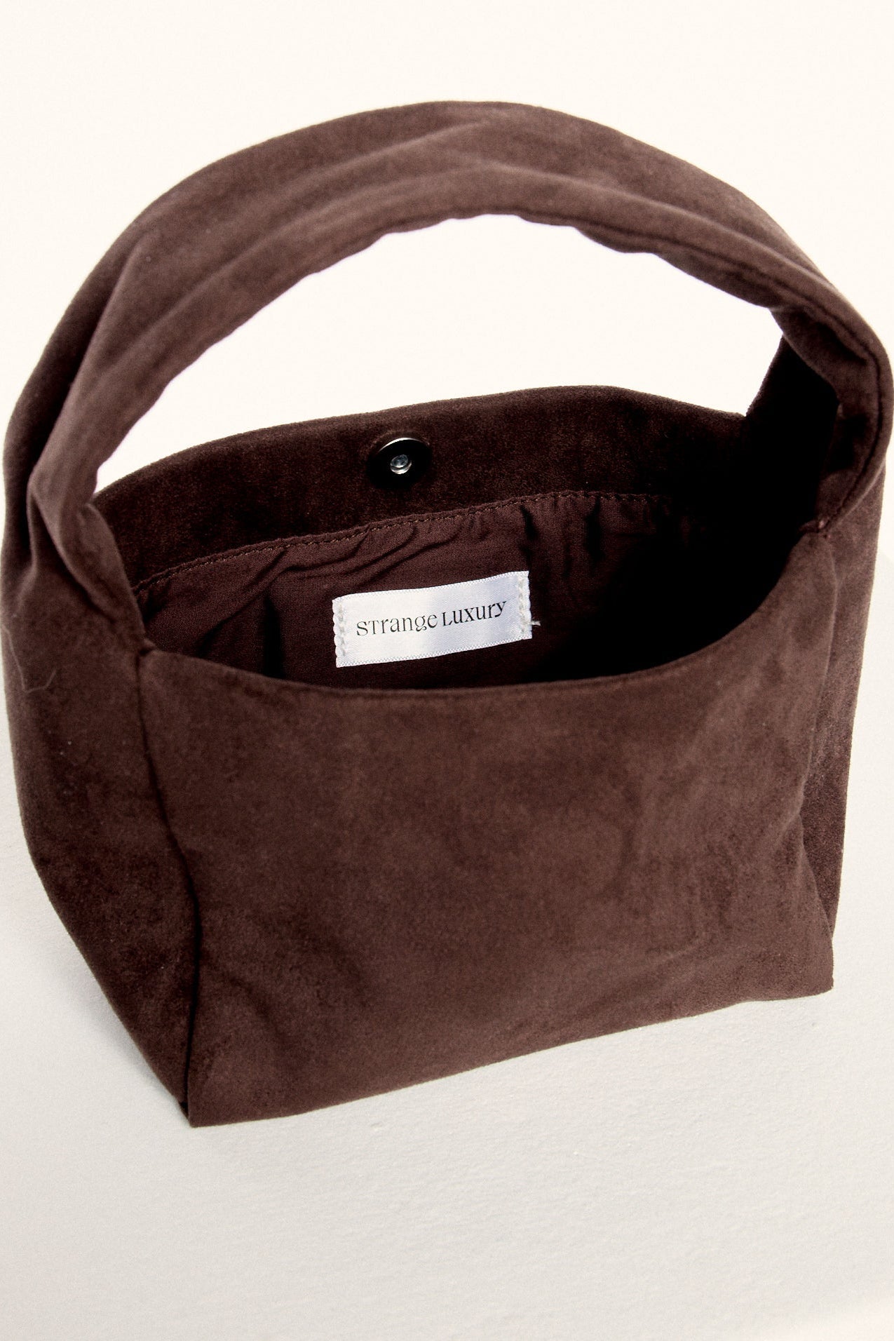 Brown suede handbag with a visible brand label on a white background.
