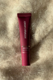 Lip balm tube on a textured beige surface.