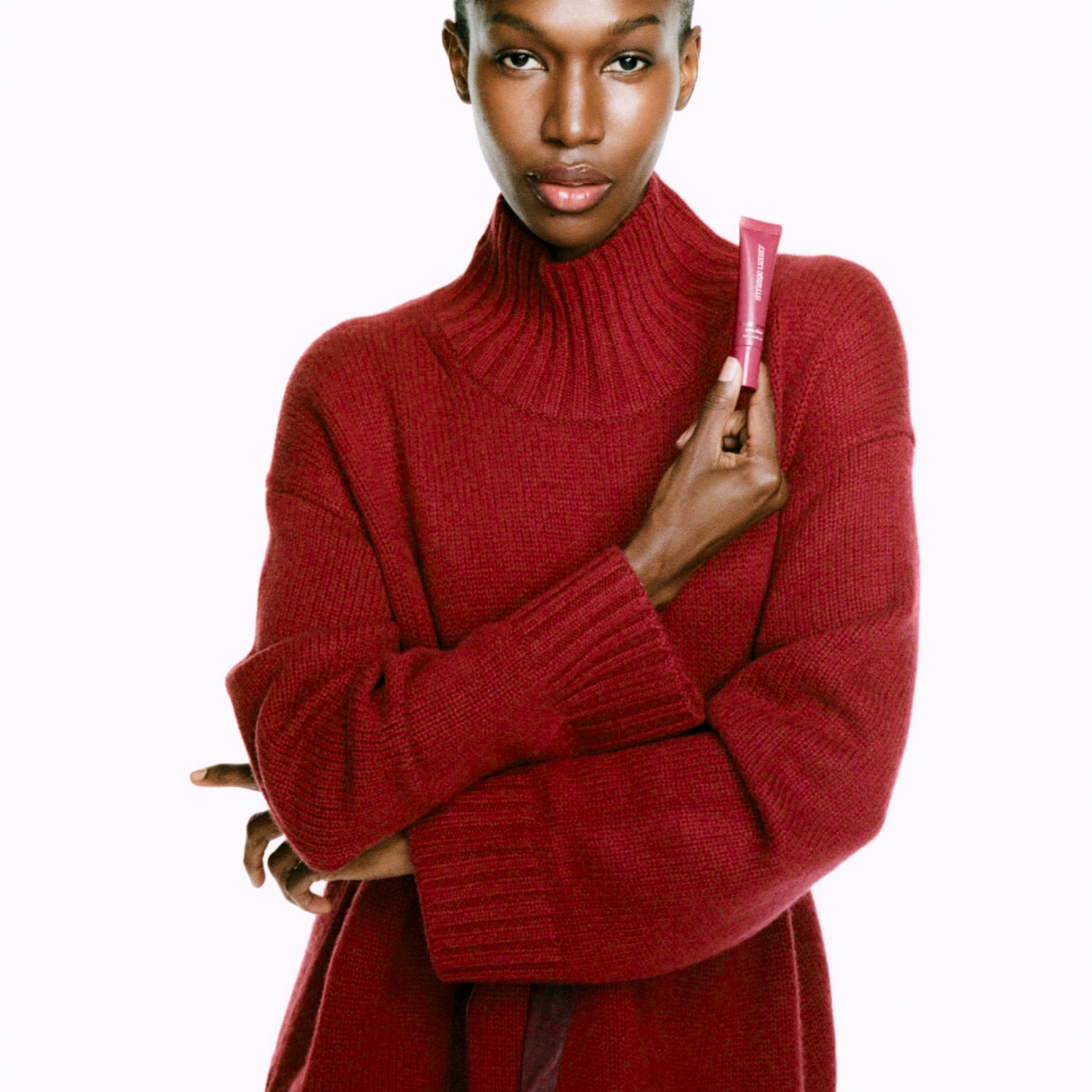 Model wearing a red sweater holding a Cashmere Lips tube a white background.