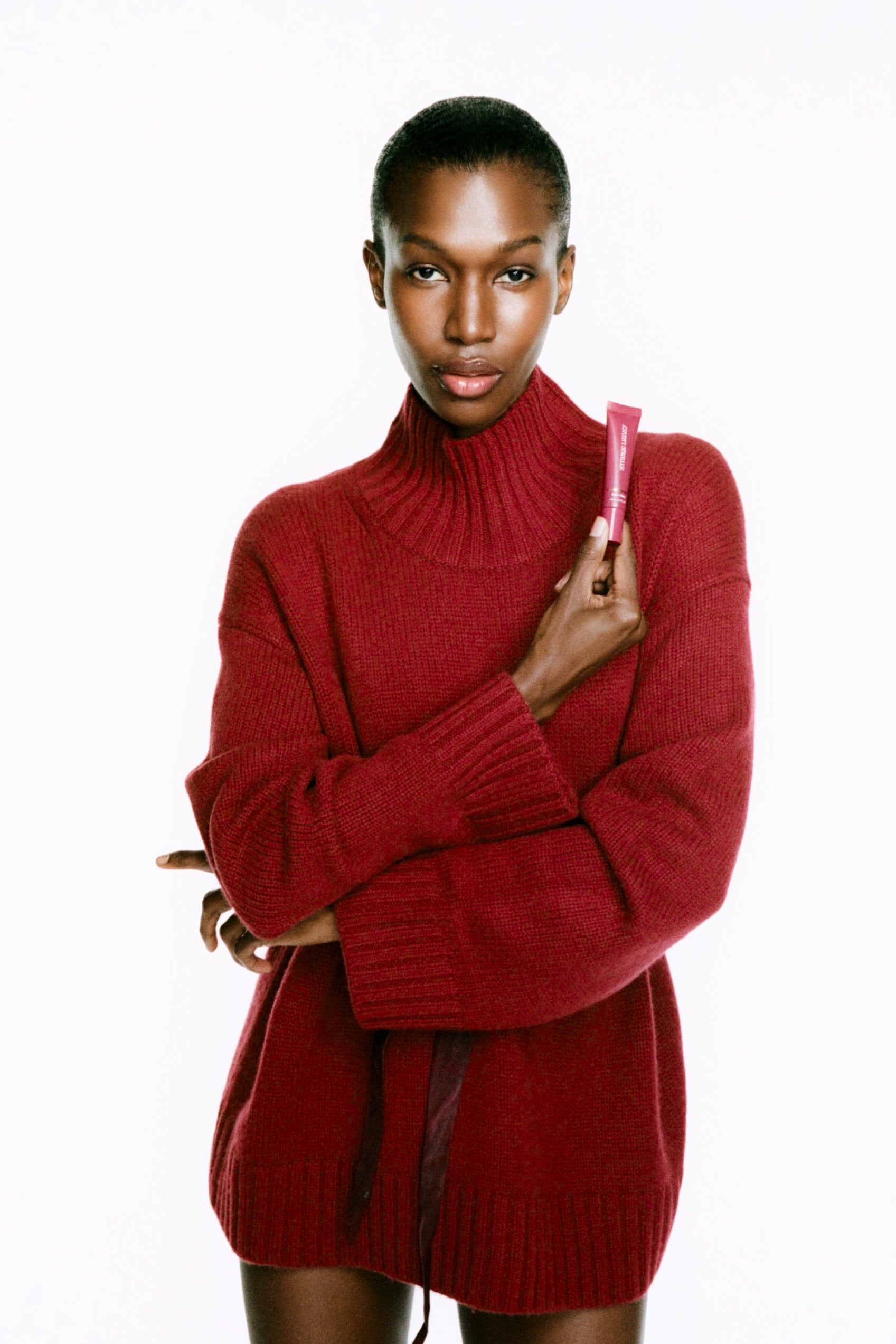 Model wearing a red sweater holding a Cashmere Lips tube a white background.