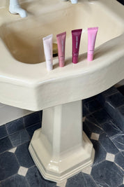 Four pink skincare tubes on a beige pedestal sink.