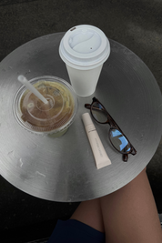 Two coffee cups, a tube of lip balm, and sunglasses on a round metal table.