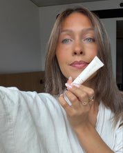 Maddie holding a lip product in a neutral indoor setting.