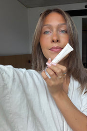 Maddie holding a lip product in a neutral indoor setting.