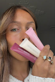 Maddie holding three Cashmere Lip products close to her face with a dark background.