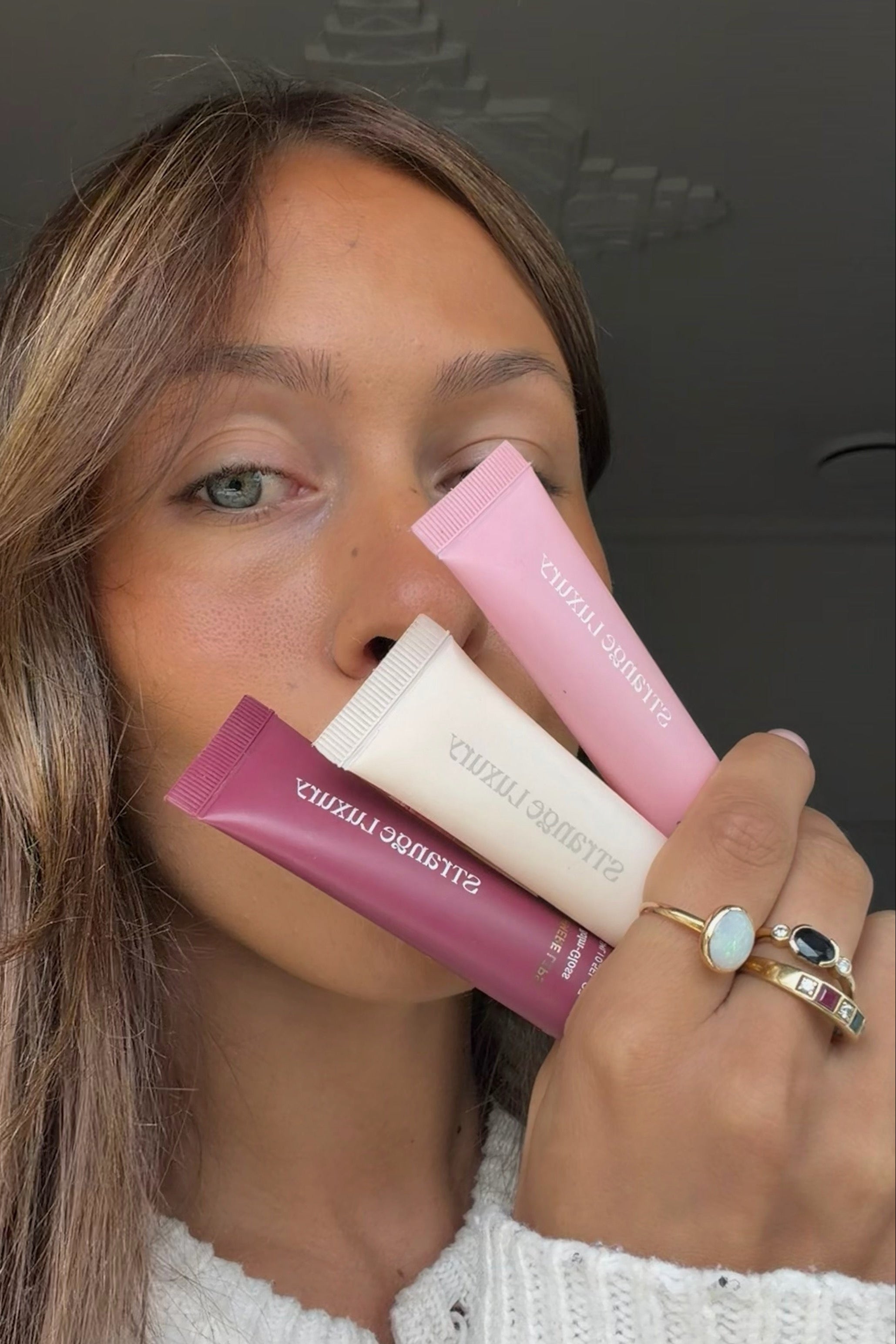 Maddie holding three Cashmere Lip products close to her face with a dark background.