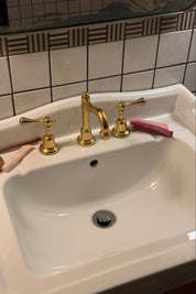 White sink with gold faucet and handles on a tiled bathroom wall with lip products.