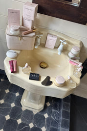 Vintage-style sink with various Strange Luxury skincare products on a tiled floor.