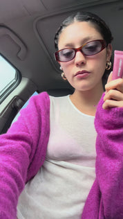 Amber applying lip product in car in purple cardigan.